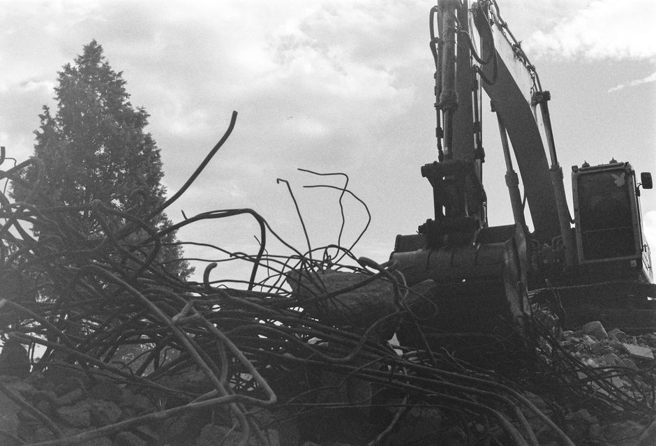 Monochrome image of an excavator engaged in demolition amidst rubble and debris.