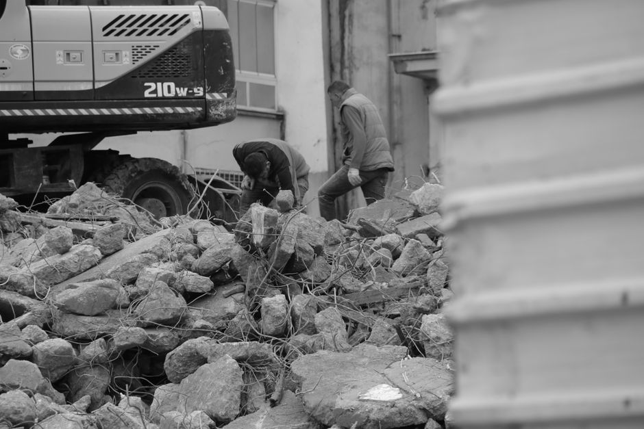 Black and white photo of workers and heavy machinery at a demolished construction site.